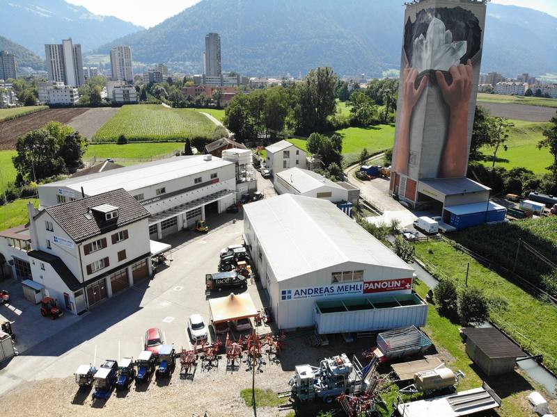 Luftaufnahme der Rheinmühle in Chur mit dem Silo-Turm, den Werkstätten und der Halle, im Hintergrund die Stadt und die Berge