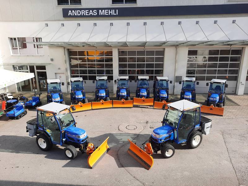 Rund zehn blaue Iseki-Kompakttraktoren mit orangen Schneepflügen stehen im Halbkreis vor der Werkstatt von Andreas Mehli in Chur