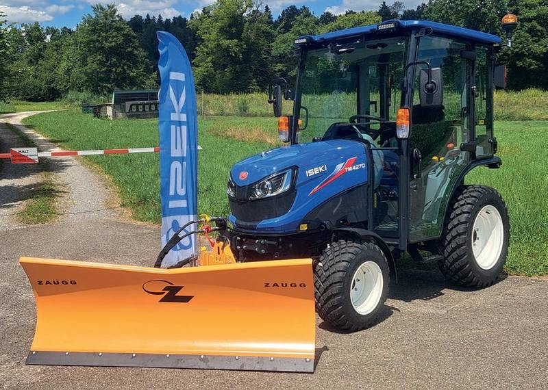 Blauer Iseki-Kompakttraktor mit Kabine und orangem Zaugg-Schneepflug auf einer Strasse