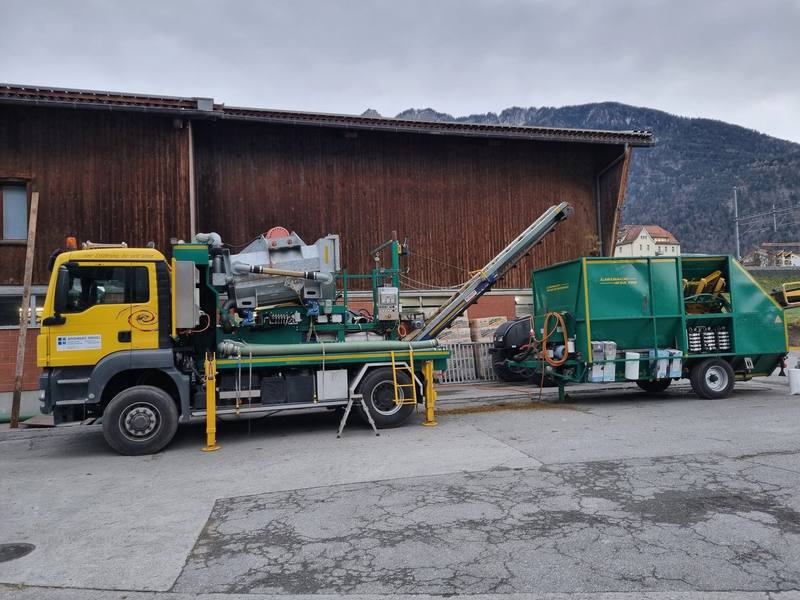 Gelber Lastwagen mit aufgebautem Separator und angehängter grüner Ballenpresse auf einem Hof
